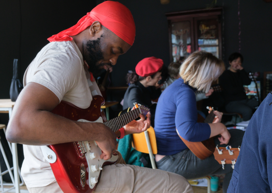 Man playing electric guitar in a class with more people.