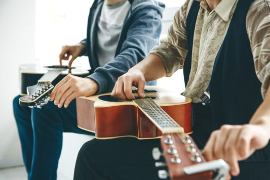 Twp people tuning their acoustic guitars on their laps.